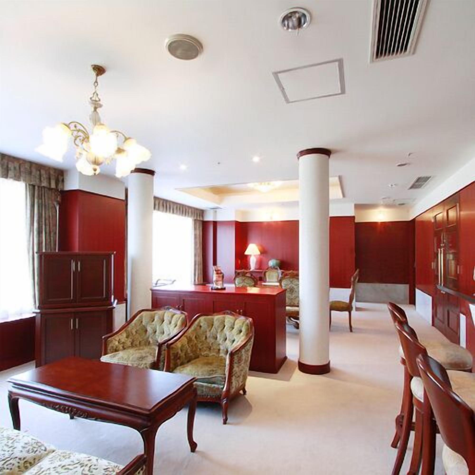 A room with a wooden table, two upholstered chairs, a chandelier, and a red accent wall.