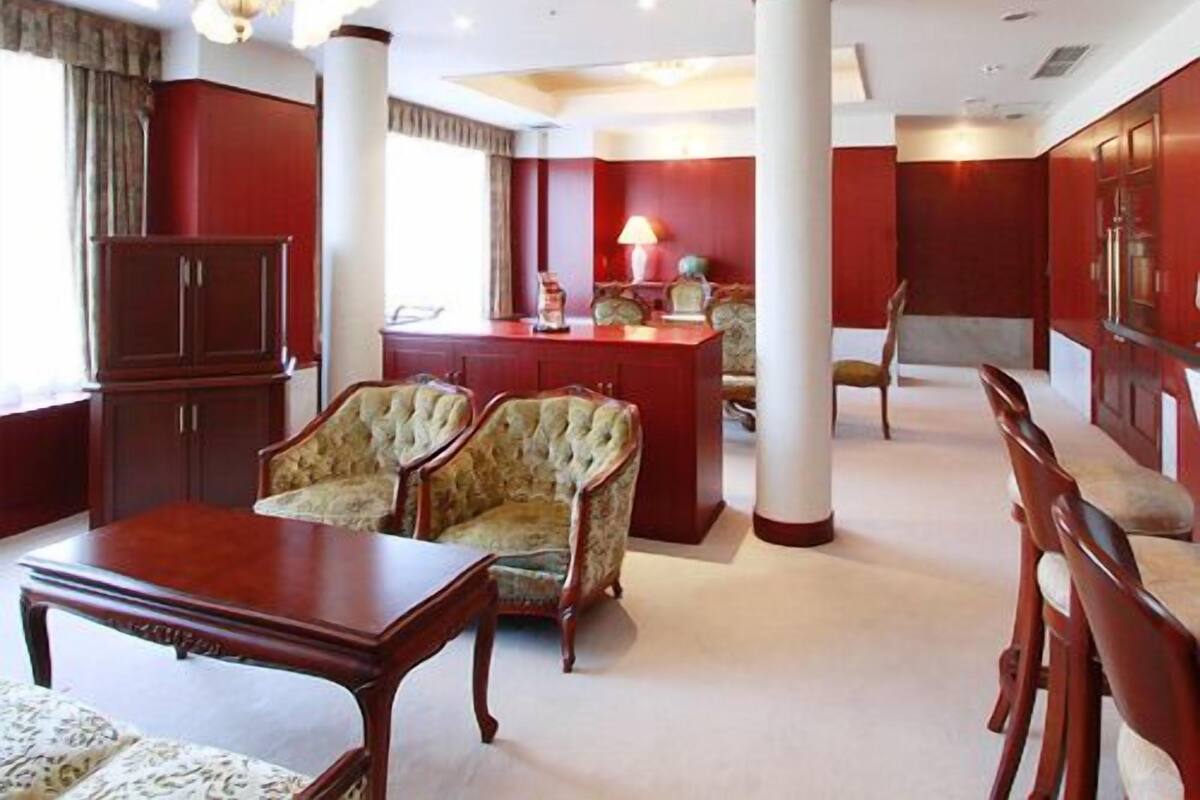 A room with a wooden table, two upholstered chairs, a chandelier, and a red accent wall.
