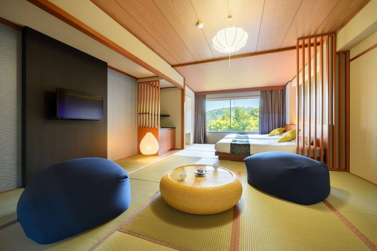 A traditional Japanese-style room with tatami flooring, a bed with pillows, a television, a lamp, and a view of greenery outside.