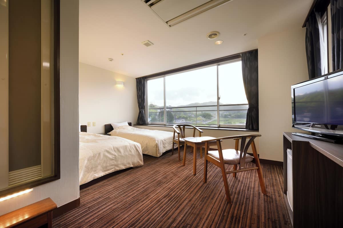 Ein Hotelzimmer mit zwei Betten, einem Schreibtisch mit Stuhl, einem Fernseher und einem großen Fenster mit Blick.