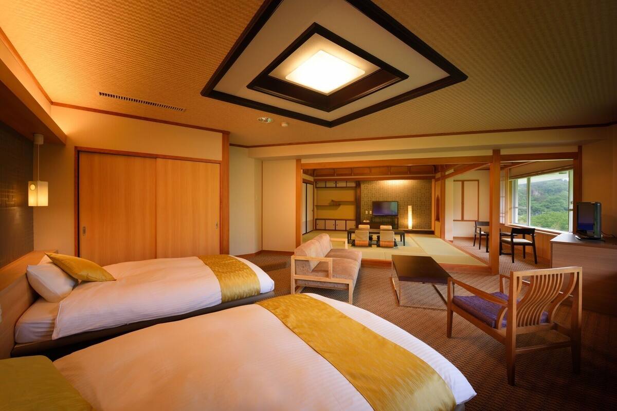 A hotel room with two beds, a seating area with a TV, and a view of the outdoors.