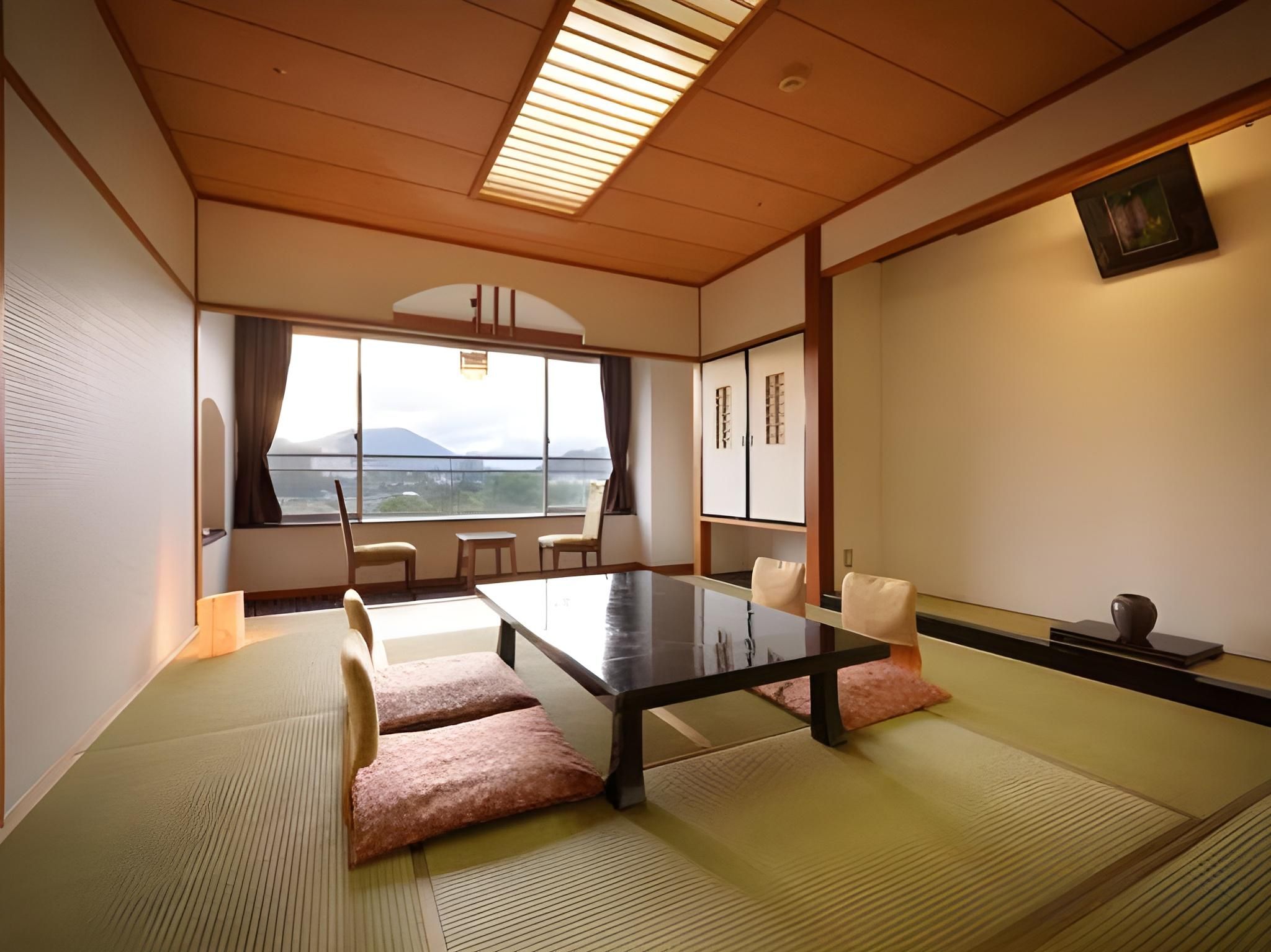 A tatami room with a low table and chairs, a view of the sea, and traditional Japanese decor.