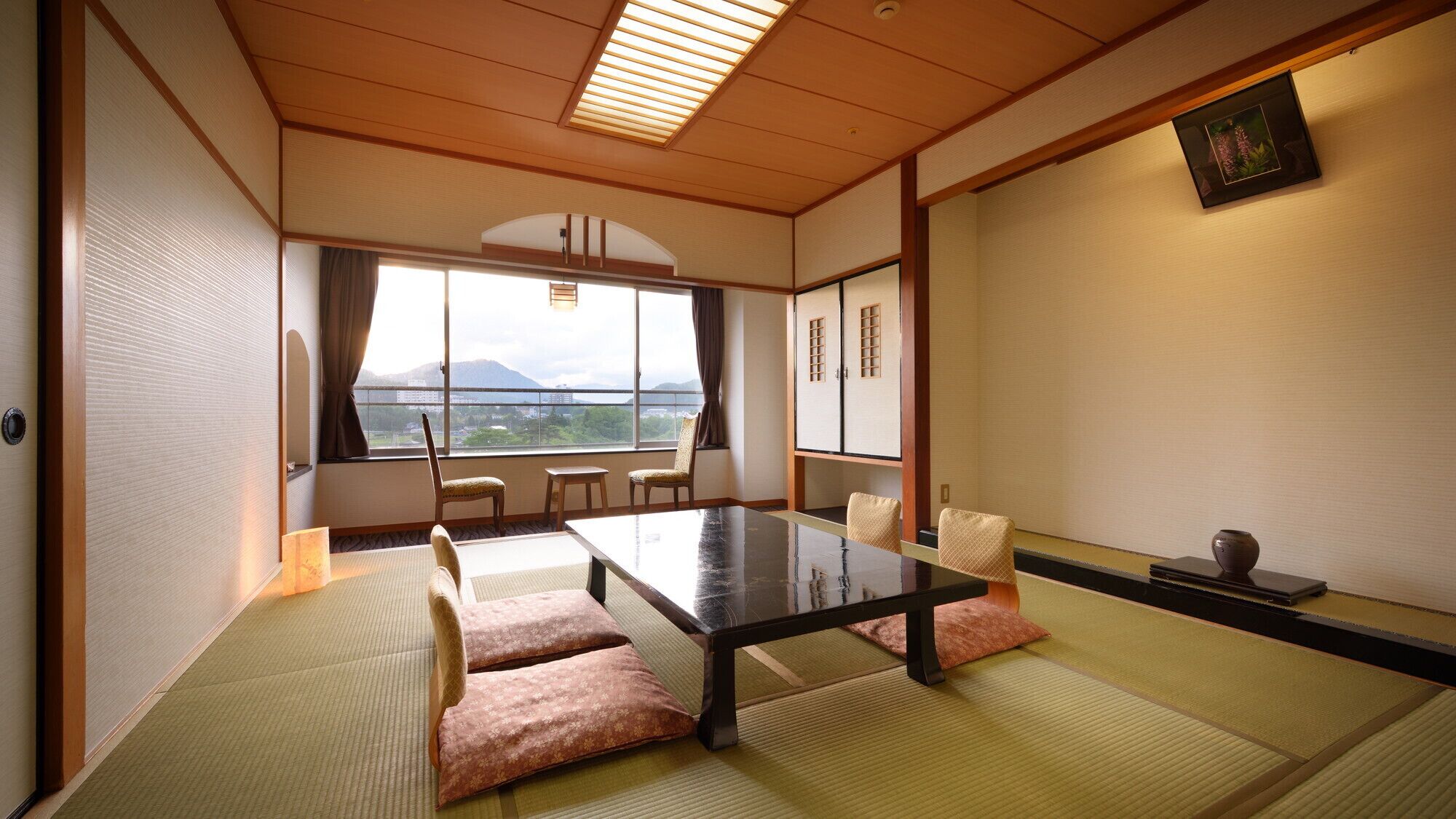 A traditional Japanese room with tatami flooring, a low table, and a view of mountains through a large window.