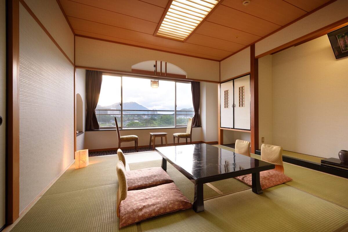 A traditional Japanese room with tatami flooring, a low table, and a view of mountains through a large window.