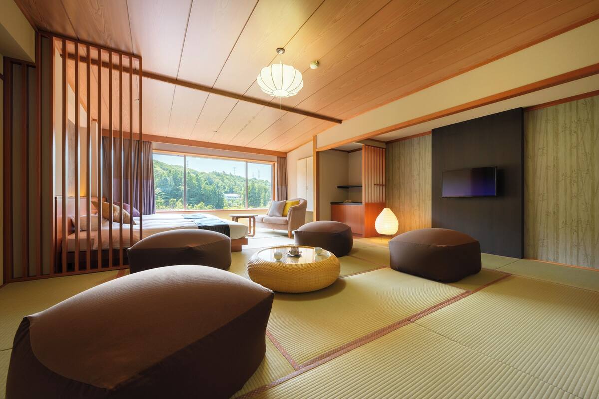 A traditional Japanese room with tatami flooring, low wooden furniture, and a television on the wall.
