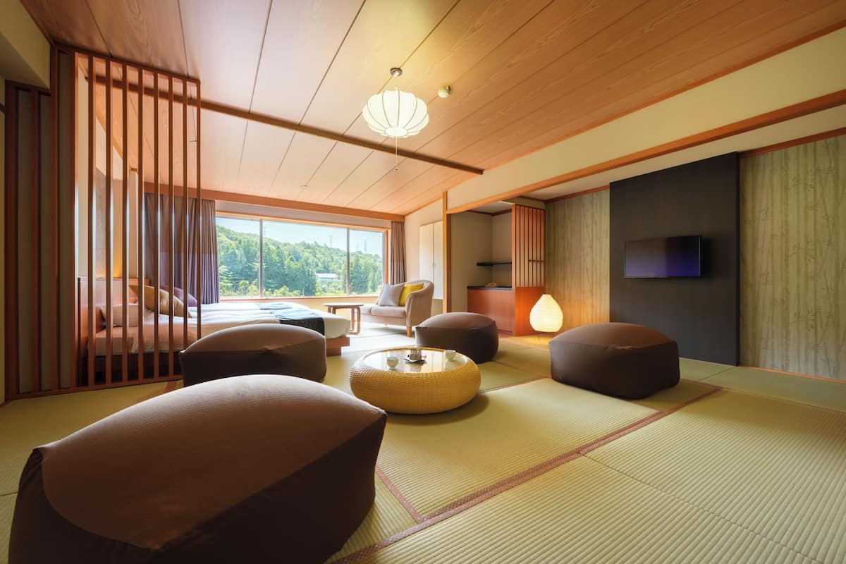 Ein traditioneller japanischer Raum mit Tatami-Bodenbelag, niedrigen Holzmöbeln und einem Fernseher an der Wand.