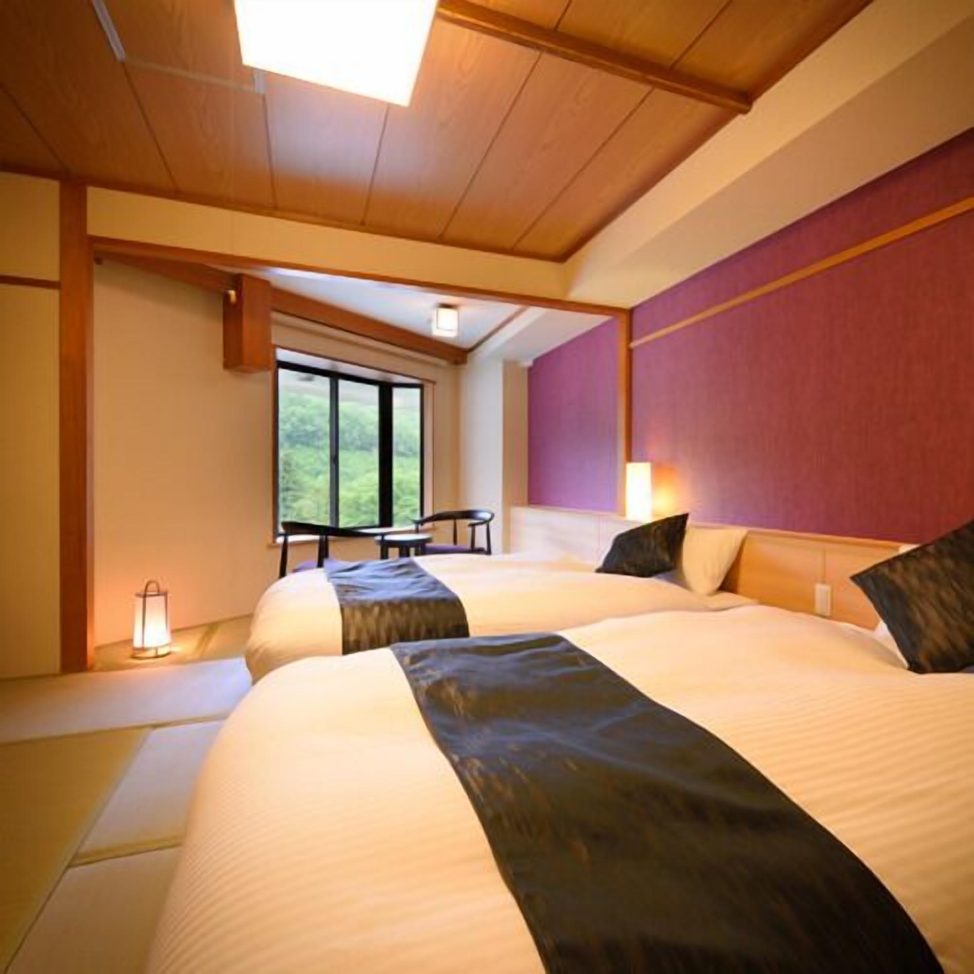 A hotel room with two beds, a window, a table, and a chair.