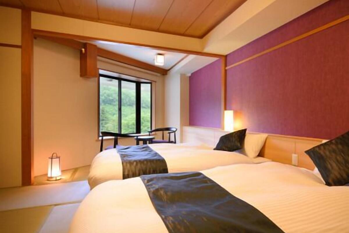 A hotel room with two beds, a window, a table, and a chair.