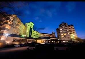 A multi-story hotel with a modern design, featuring a prominent green-lit tower and a unique building structure on the right.
