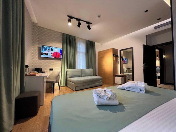 Une chambre d’hôtel moderne équipée d’un lit, d’un bureau, d’un canapé et d’un téléviseur fixé au mur.