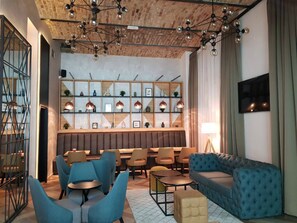 A modern lounge area with a high ceiling, exposed brick, and a mix of seating options including sofas and chairs. - Hotel Capital (Belgrade)