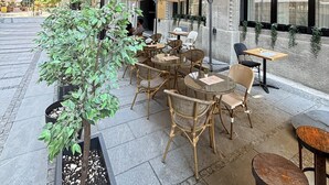 An outdoor seating area with wicker chairs and tables, a potted plant, and a building with a sign for the Capital Hotel. - Hotel Capital (Belgrade)