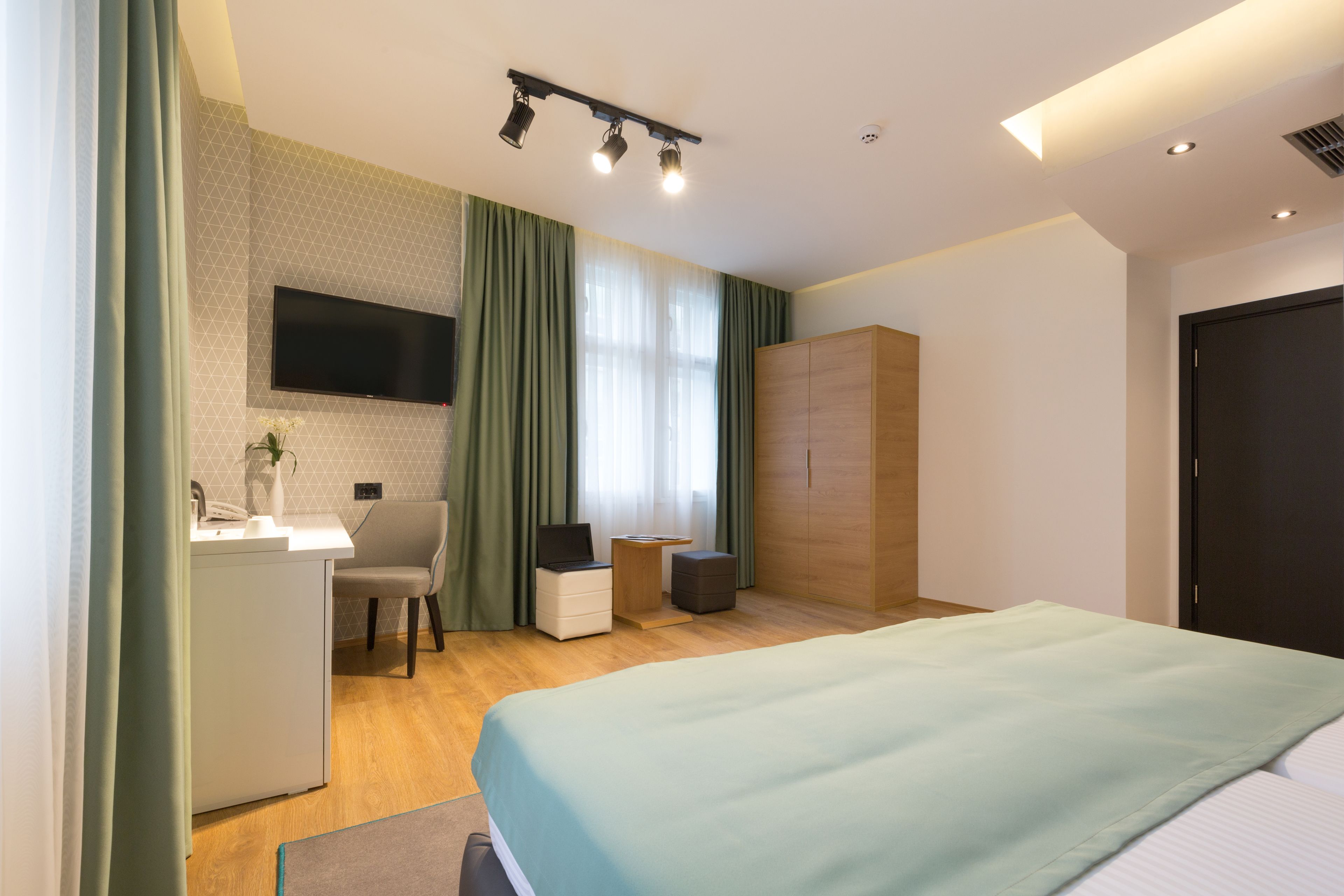 A modern hotel room with a bed, desk, chair, and wardrobe.