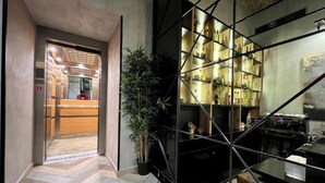 A modern hotel lobby with a herringbone patterned floor, a reception desk, and a glass partition with shelves displaying bottles. - Hotel Capital (Belgrade)