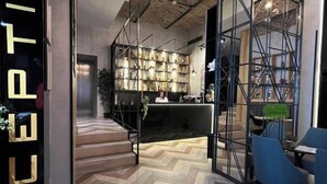 A reception area with a herringbone patterned floor, a glass door with the word "RECEPTION" on it, and a modern interior with a metal shelving unit and blue chairs. - Hotel Capital (Belgrade)