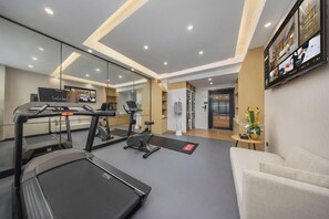 A modern hotel room with a treadmill, exercise equipment, a sofa, a dining area, and a mirror reflecting the room. - Vienna International Hotel (shenzhen Wangzhong Cit (Shenzhen)