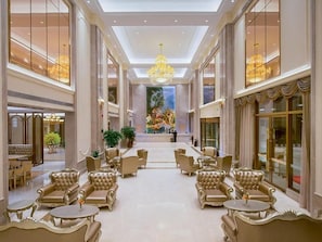Un vestíbulo amplio con techos altos, candelabros y una zona de estar central con sillones y mesas tapizadas.