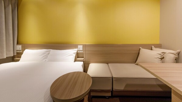 A hotel room with two beds, a wooden nightstand, a round table, and a yellow accent wall. - Via Inn Shimonoseki (Shimonoseki)
