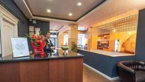 A hotel reception area with a wooden reception desk, a framed certificate, and a bouquet of flowers.