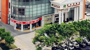 A modern building with a curved glass facade, a central entrance with columns, and a parking lot with cars. - Vienna Hotel Foshan Nanhai Avenue Branch (Foshan)