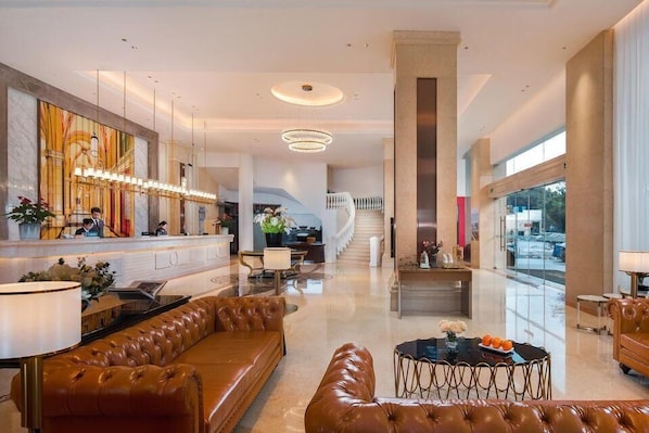 A spacious lobby with a reception desk, leather seating, a staircase, and large windows.