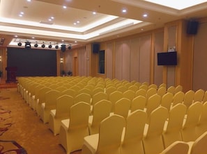 A conference room with rows of yellow chairs, a podium, and a large screen.