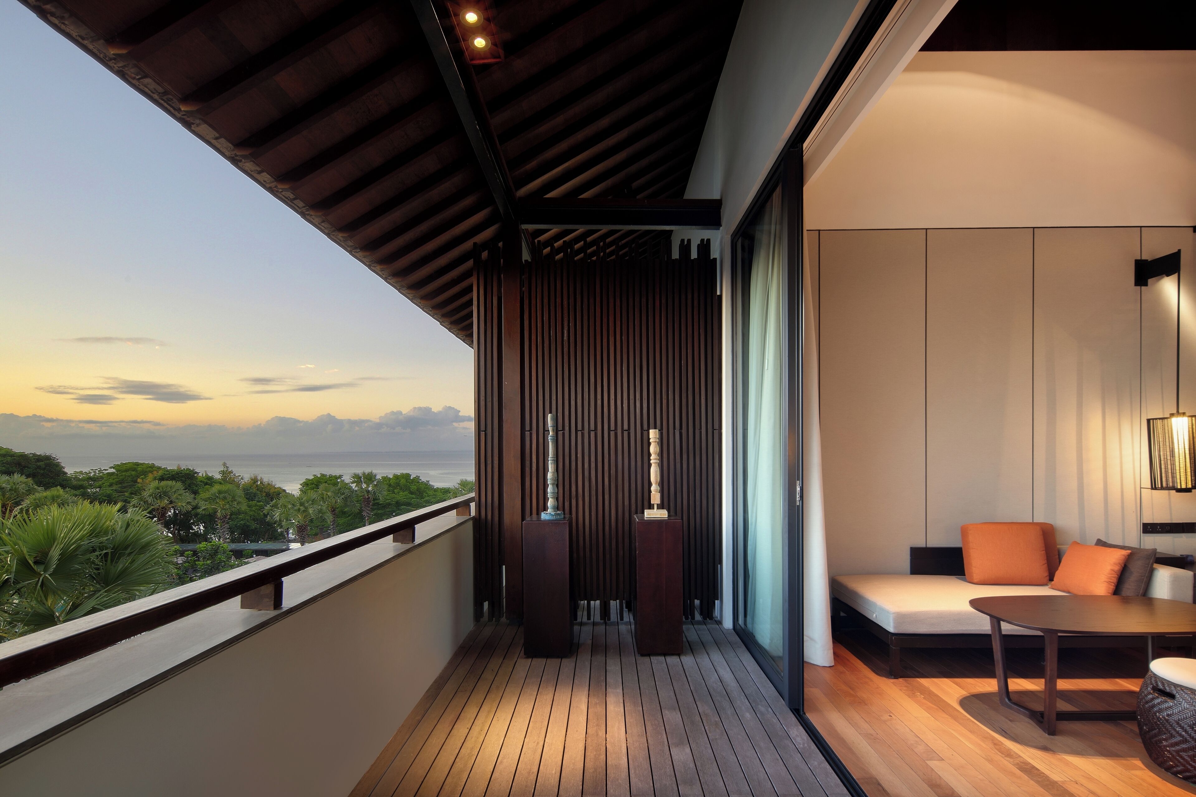 A balcony with a wooden floor, a sofa with cushions, a table, and two decorative vases.