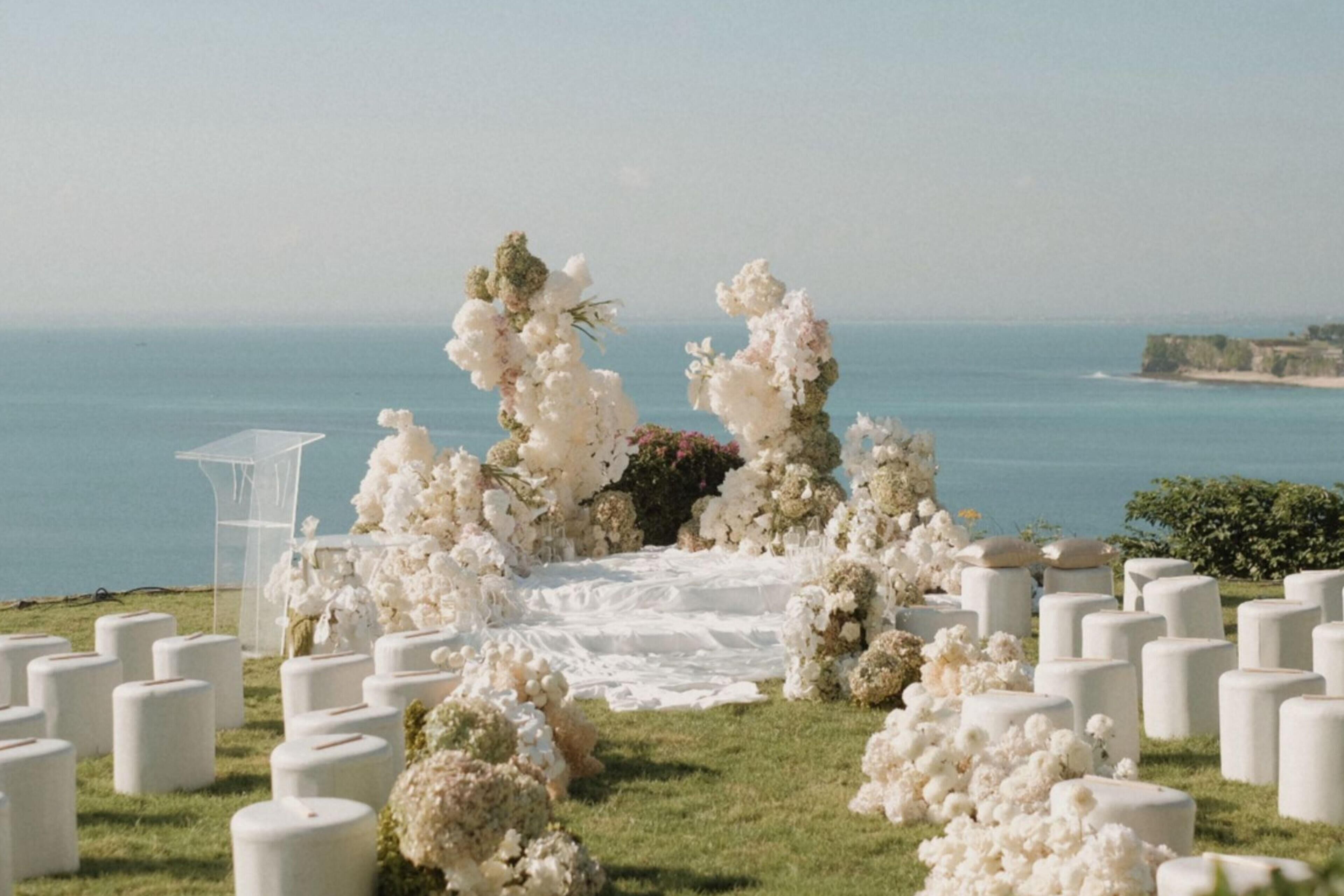 Ceremonia de boda al aire libre con vistas despejadas al mar, arreglos florales blancos y un atril.