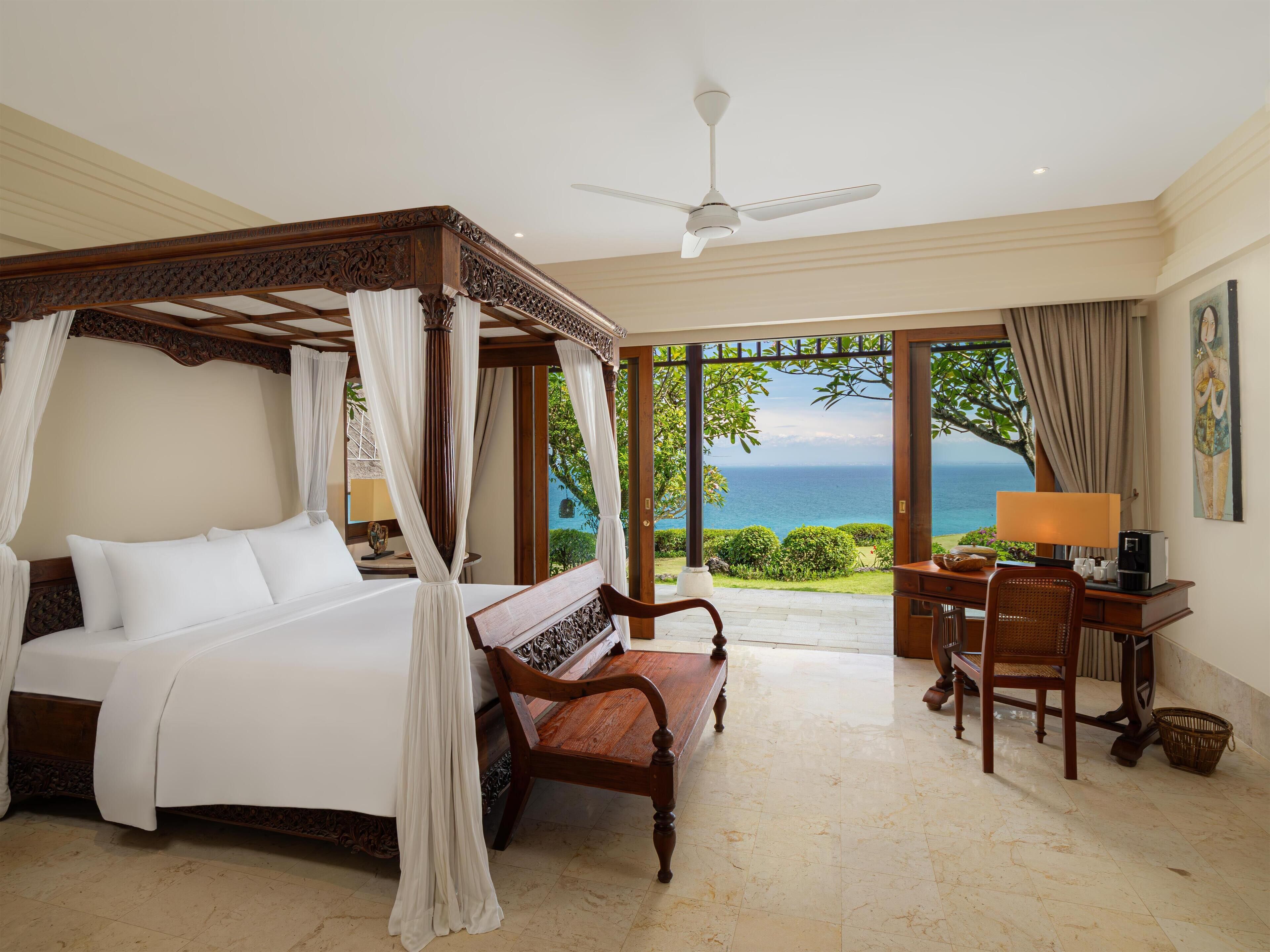 A four-poster bed with a canopy, a desk with a chair, and a view of the ocean.