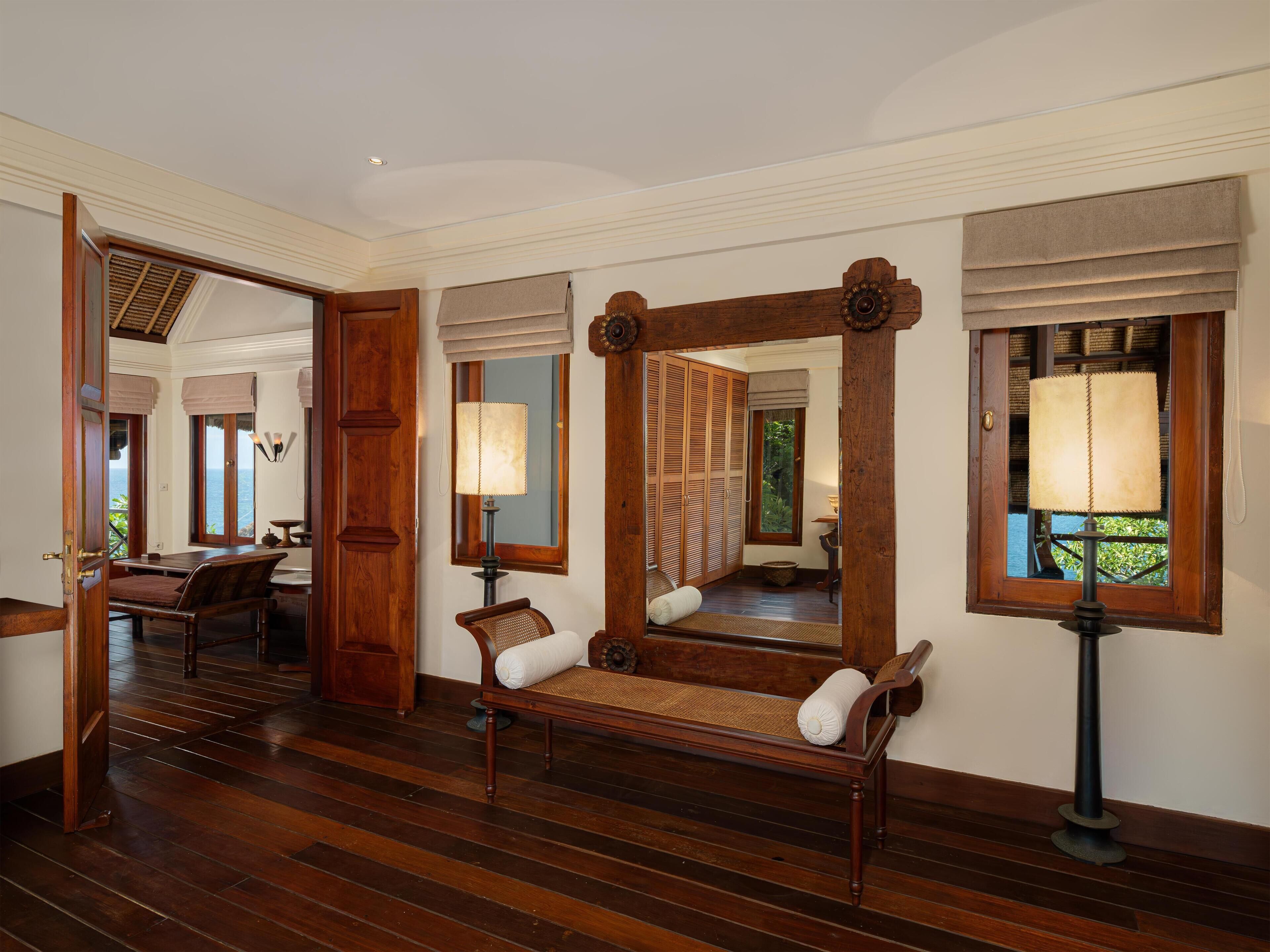 A room with a wooden floor, a bench with cushions, a mirror, and a lamp.