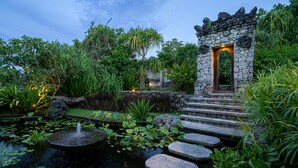 Un jardin paisible, avec un sentier de pierres menant à une petite construction en pierre dotée d’une porte éclairée.
