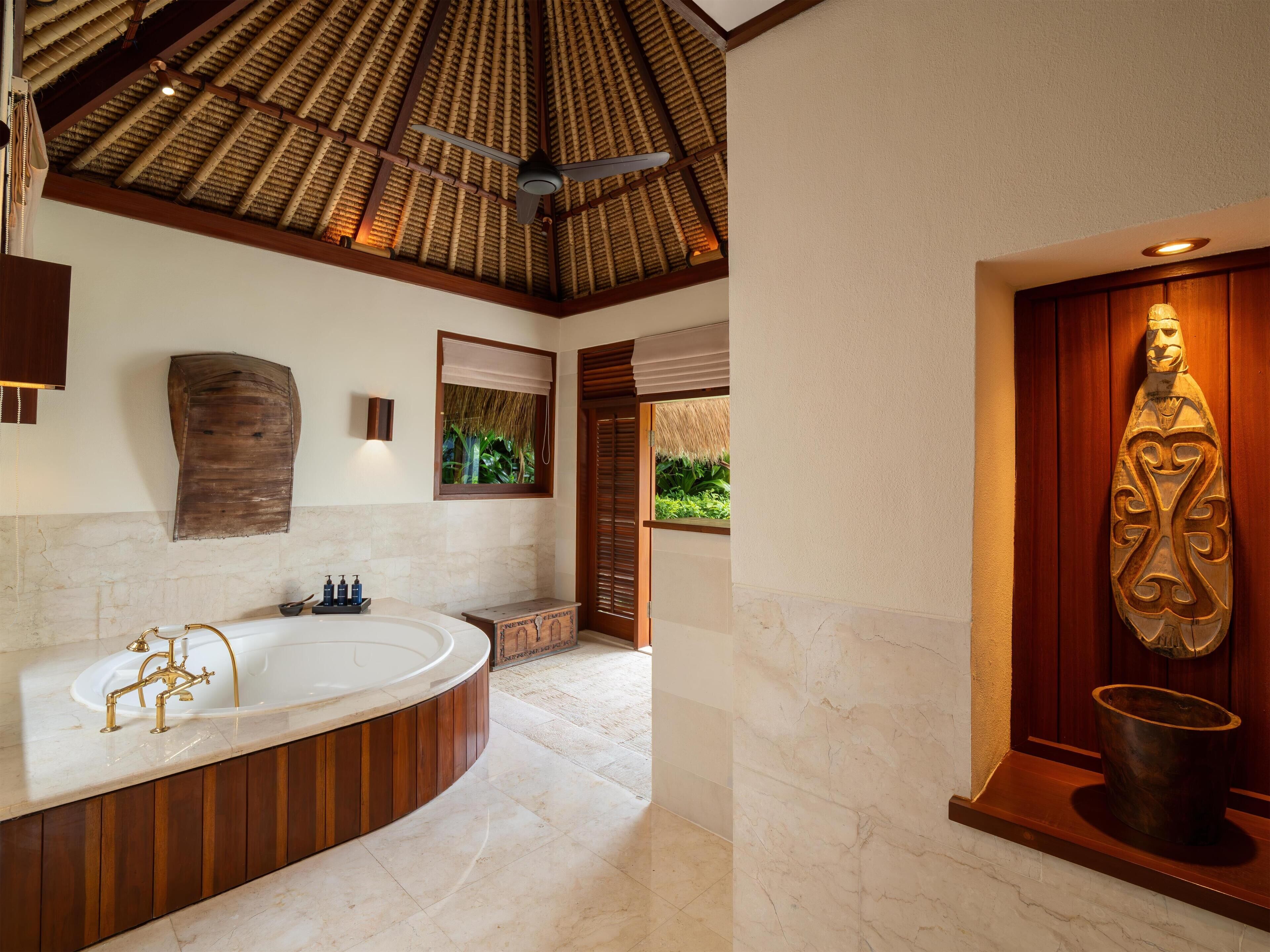 A spacious bathroom with a large bathtub, a ceiling fan, and a wooden sculpture.
