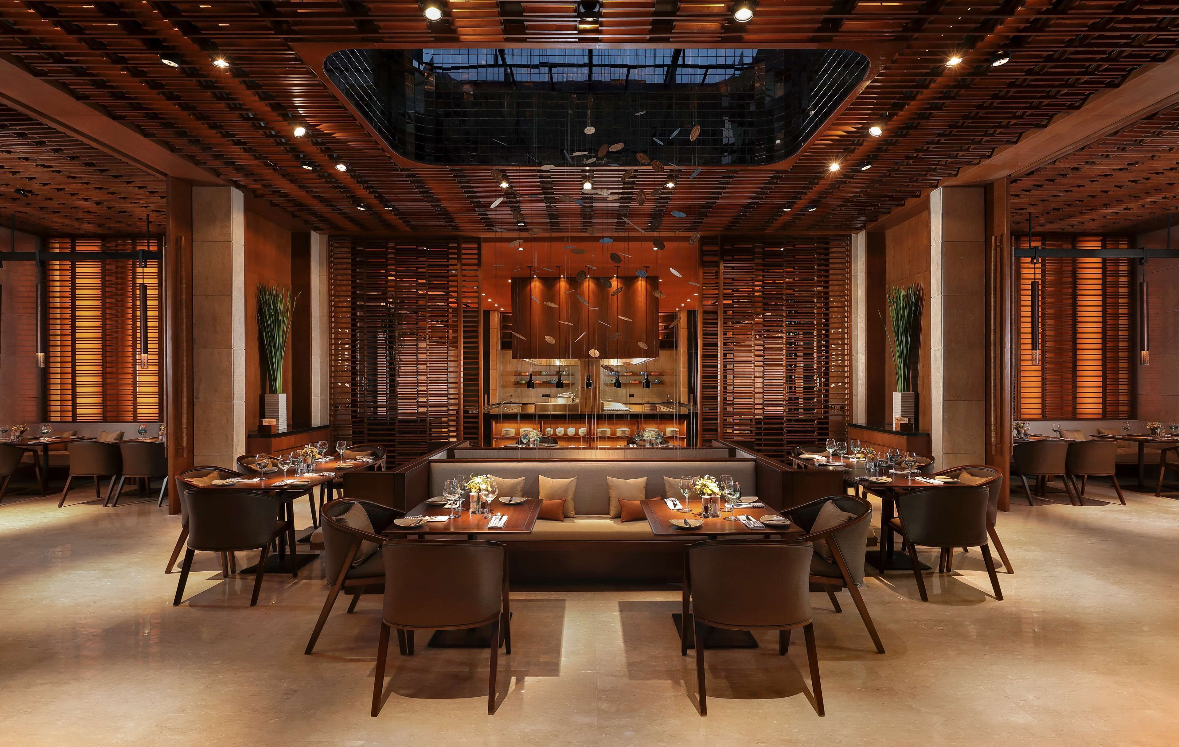 A modern restaurant with a central seating area, high ceilings with wooden beams, and a skylight.