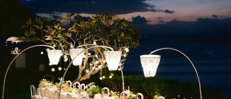 An outdoor dining setup with white chairs and tables, decorated with flowers and under white canopies.
