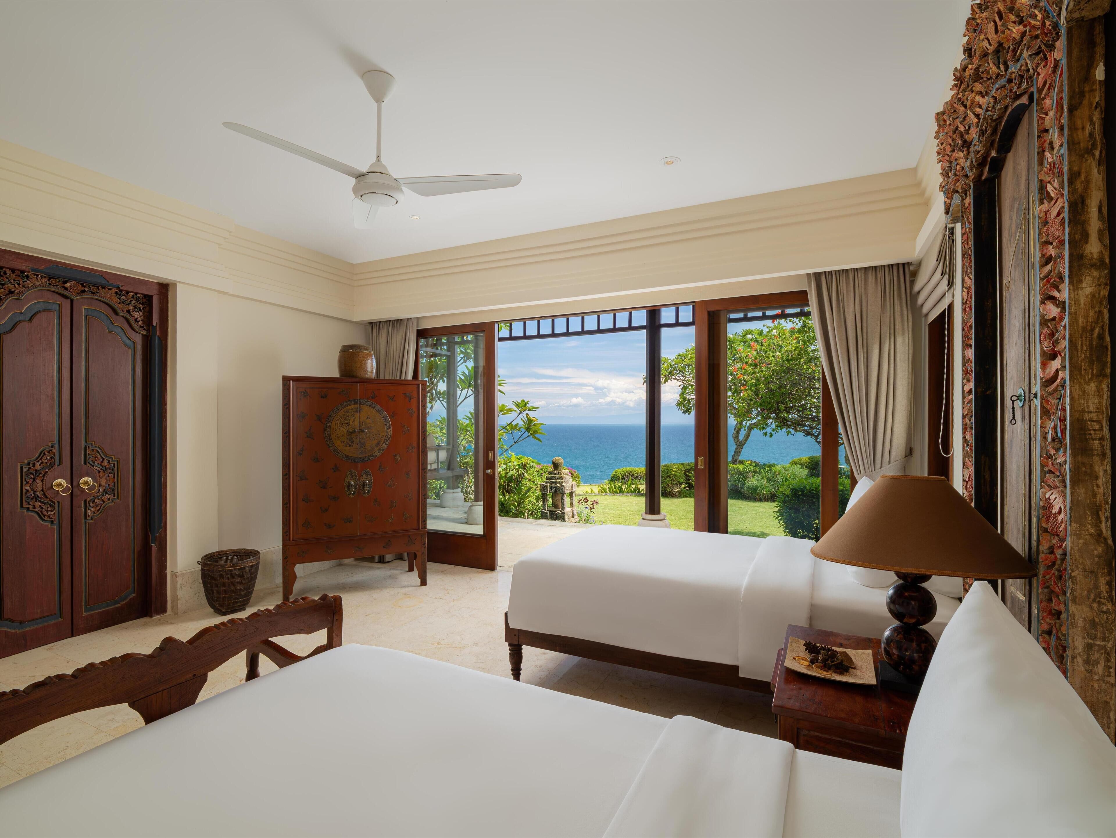 A hotel room with two beds, a ceiling fan, a wooden cabinet, and a view of the ocean.