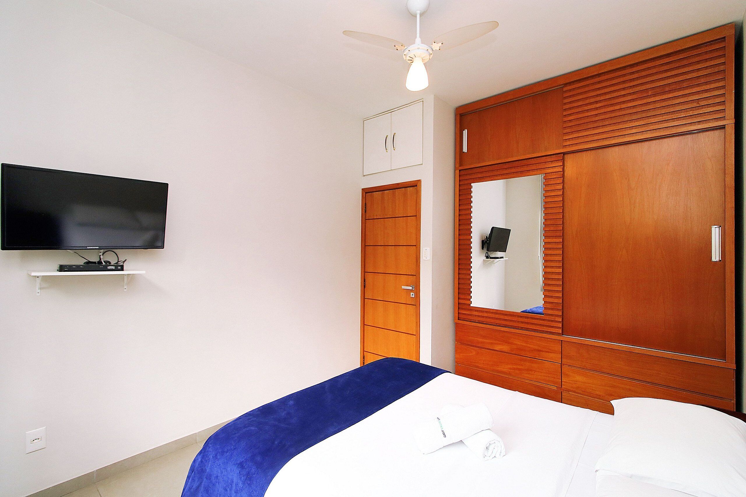 Une chambre à coucher comprenant un lit, un téléviseur fixé au mur, une armoire et un ventilateur de plafond.