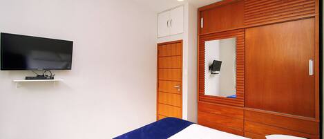 Une chambre à coucher comprenant un lit, un téléviseur fixé au mur, une armoire et un ventilateur de plafond.