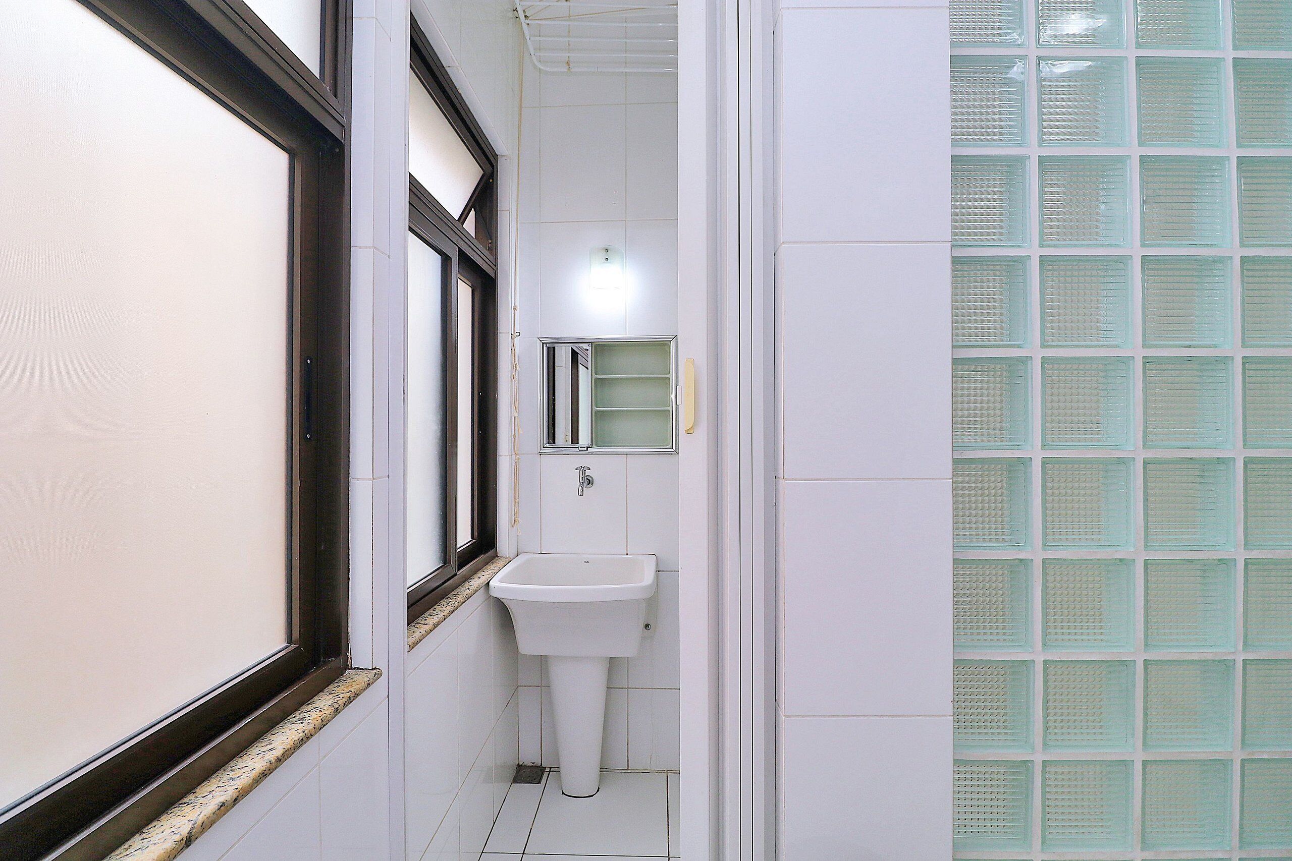 A narrow bathroom with a white sink, a mirror above it, and a window with a black frame.