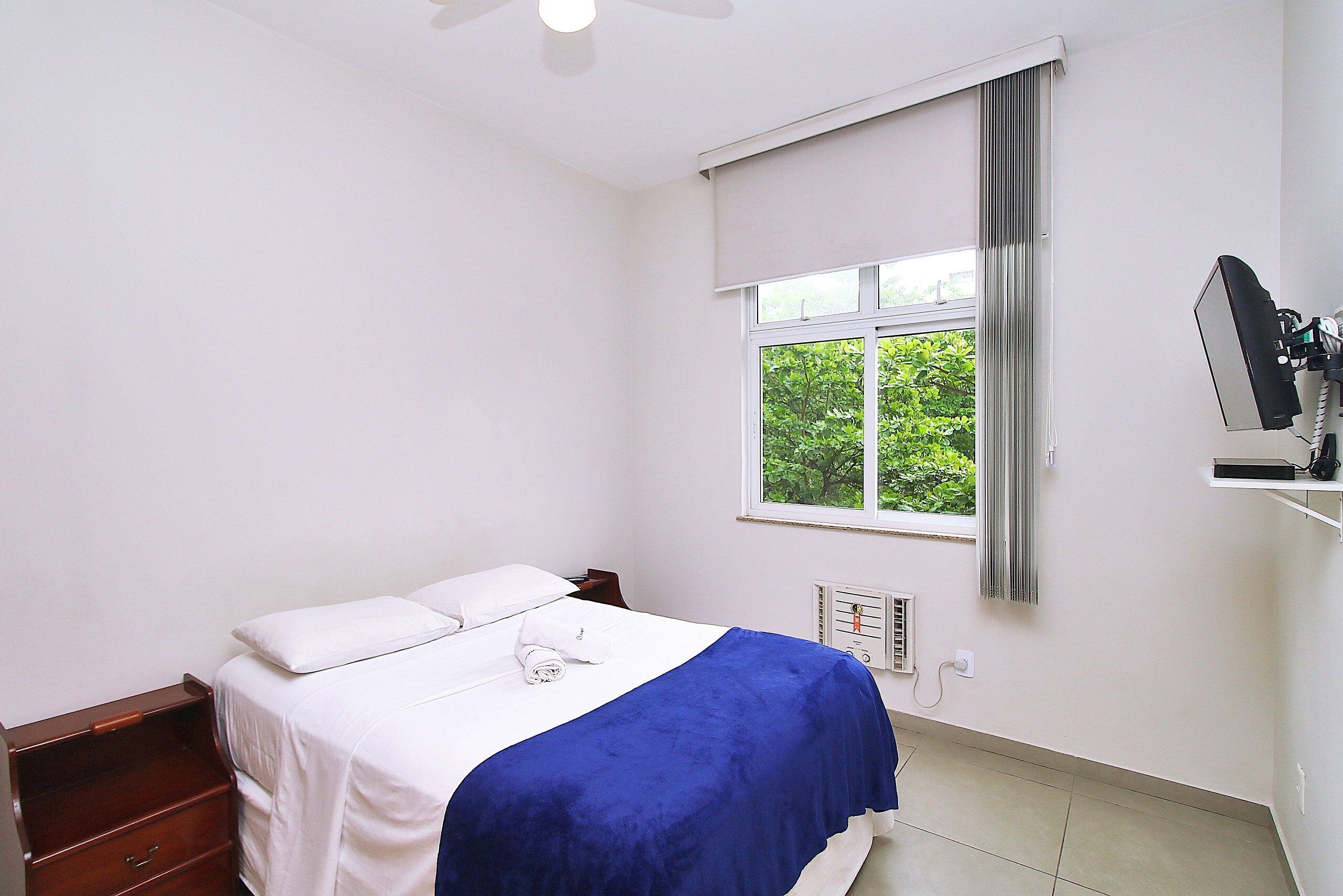 A bedroom with a bed, a nightstand, a dresser, a window with curtains, and a radiator.