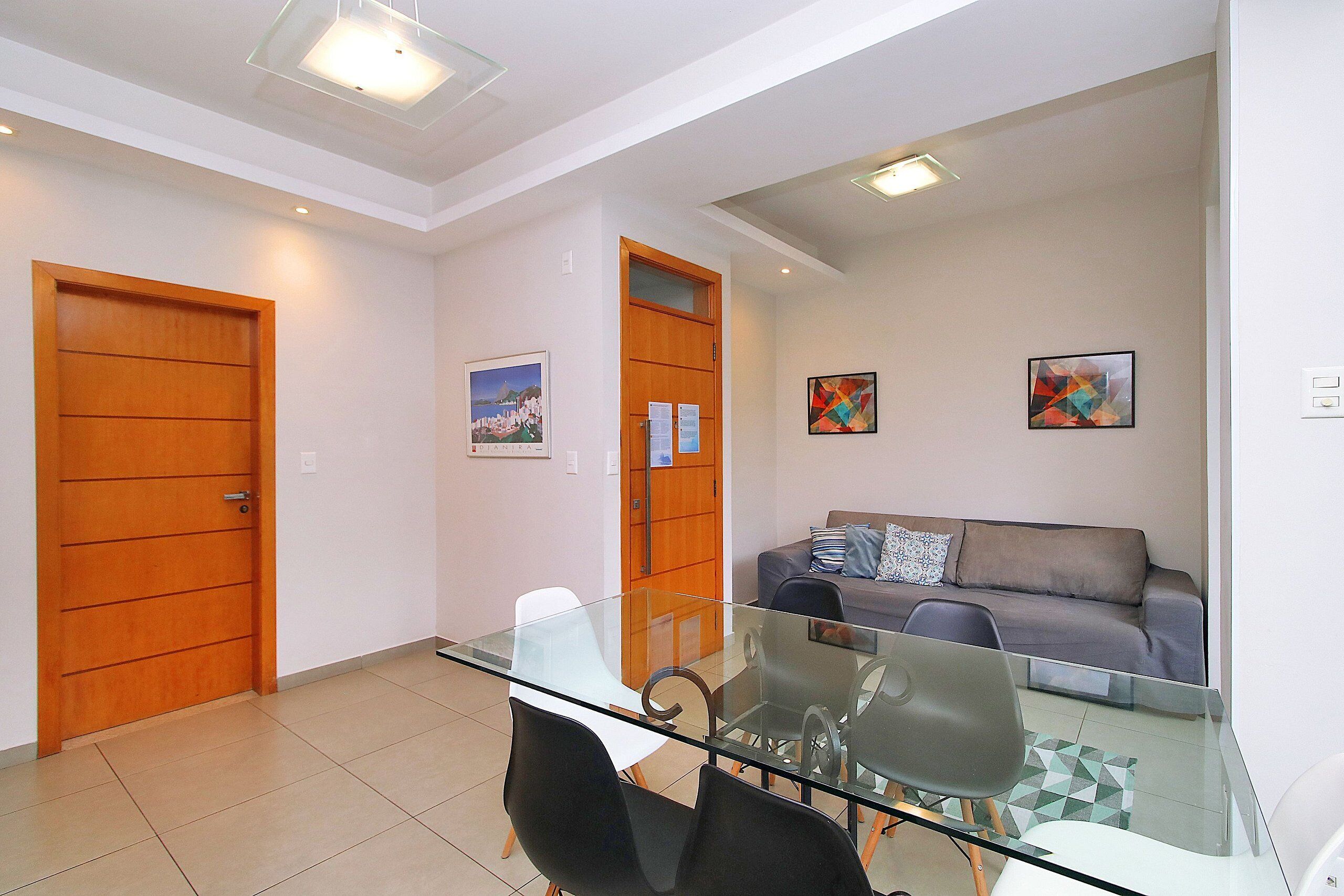 A modern living room with a glass dining table, grey sofa, and wooden doors.