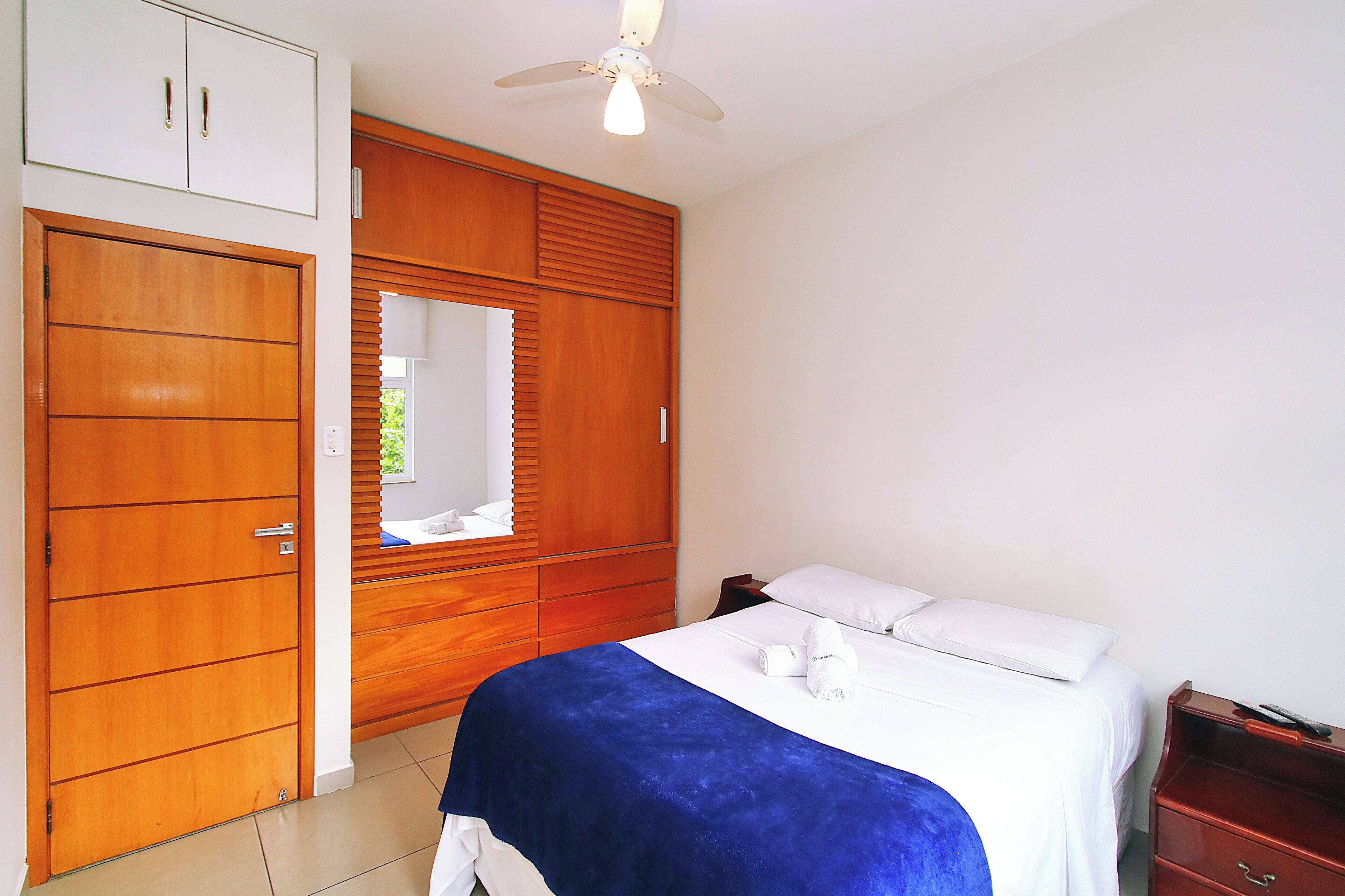 A hotel room with a bed, a wardrobe, a mirror, and a ceiling fan.