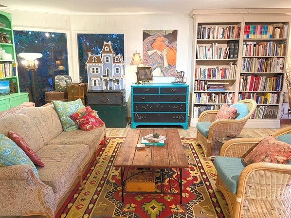 A cozy living room with a sofa, chairs, a coffee table, a bookshelf, and a painting of a house. - Wisteria Guest House (Salt Spring Island)