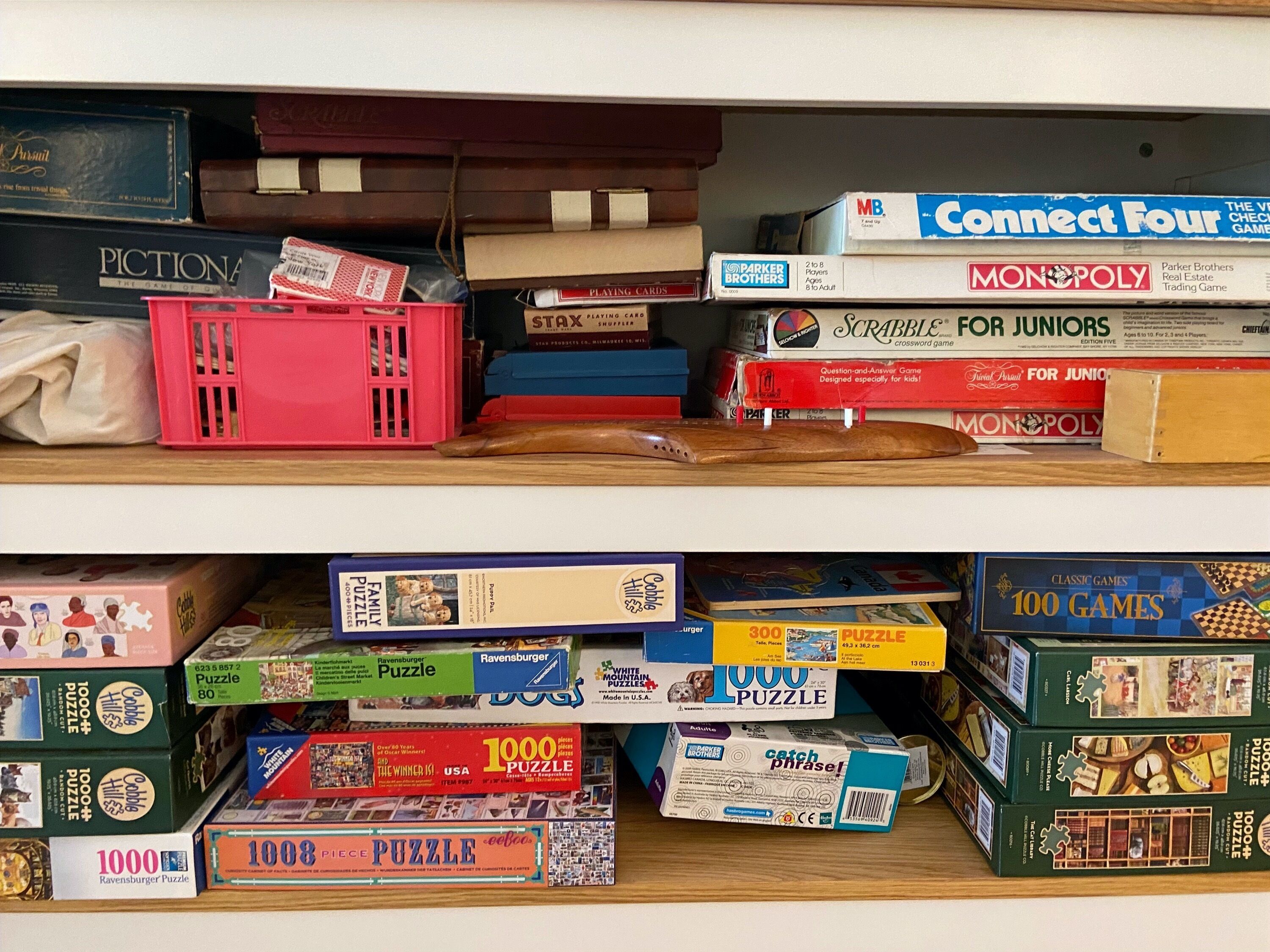 Ein Regal mit verschiedenen Gesellschaftsspielen und Puzzles, darunter Monopoly, Scrabble und Connect Four.