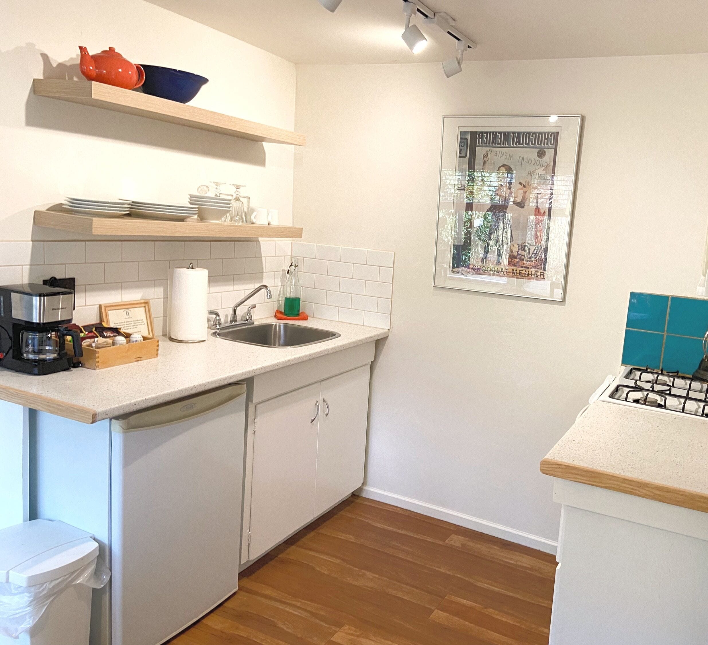 Una cocina compacta con gabinetes blancos, un lavamanos de acero inoxidable y una cafetera.