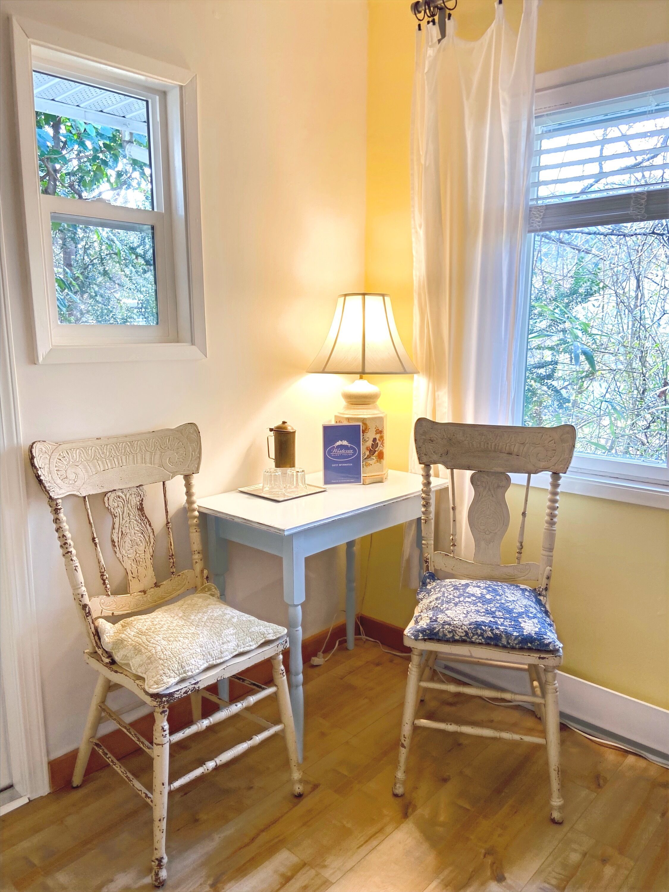 Two vintage chairs with patterned cushions, a small table with a lamp, and a window with a view of trees.