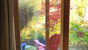 A wooden deck with a red chair and a blue table. - Wisteria Guest House (Salt Spring Island)