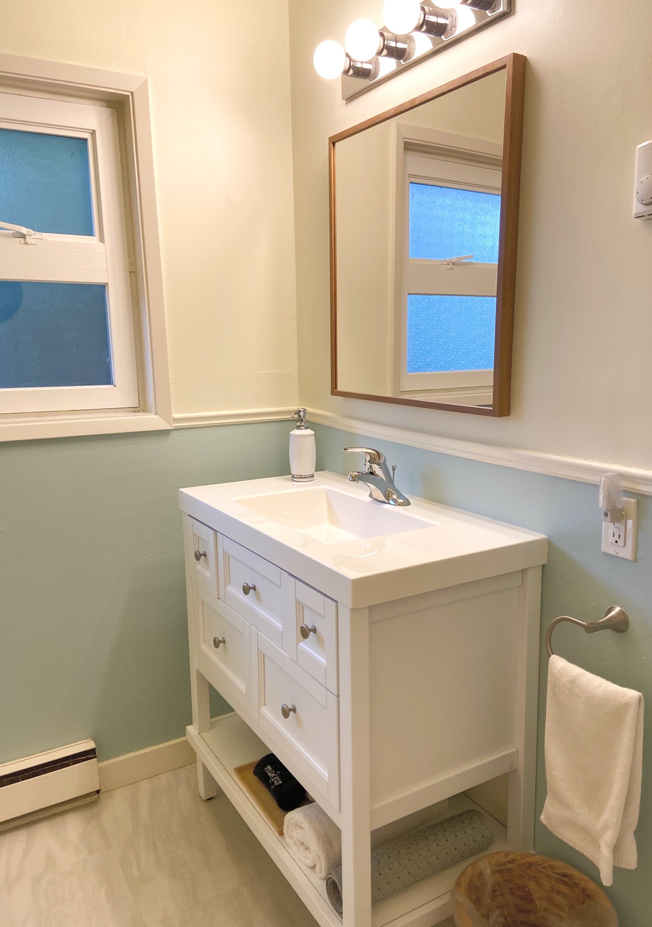 A bathroom with a white vanity, a mirror, a sink, and a towel rack.