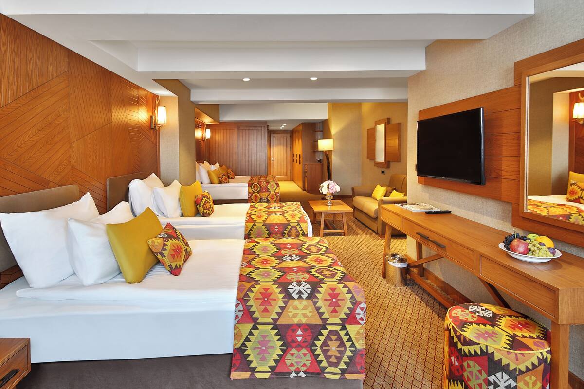 A hotel room with two beds, a TV, a desk, and a dining area.