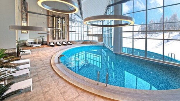 Une piscine intérieure au design incurvé, dotée de grandes fenêtres et d’un éclairage moderne.