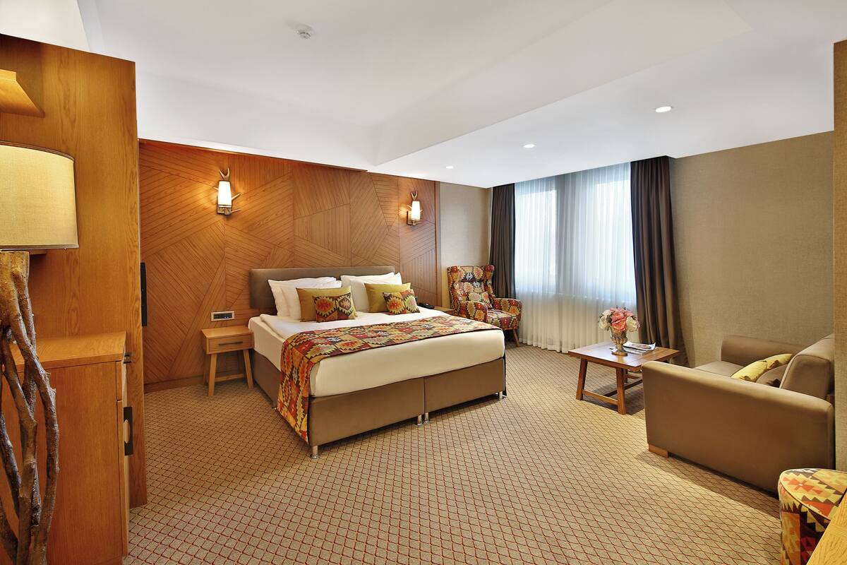 A hotel room with a large bed, a sofa, a small table with a vase, and a wooden wall panel.